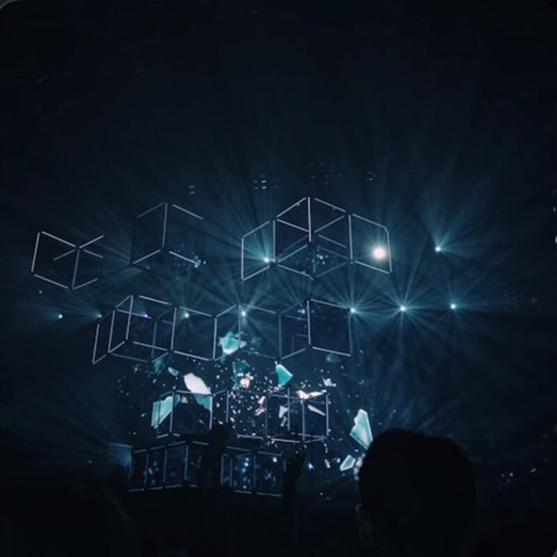 Lit cube structures suspended above a crowd at night, from the event's own listing.